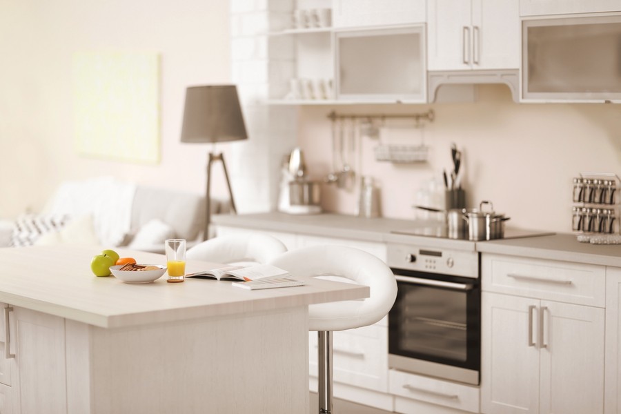 A well lit kitchen with apples and orange juice sitting in the marble island.