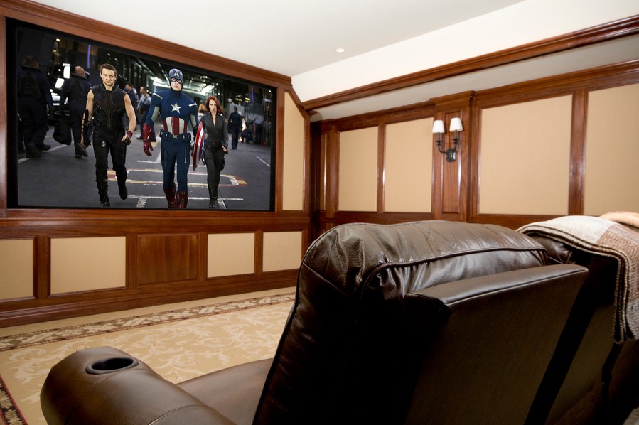 home theater with leather seats and wall-mounted screen playing a Marvel movie.