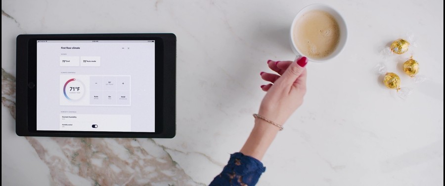 A woman’s hand reaching for a cup of coffee. A tablet with a home automation interface is next to her on the counter. 