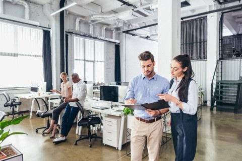 Co-workers conversing and using smart devices in a large office space.
