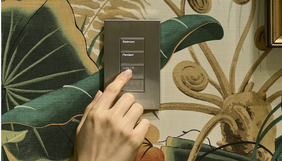 Hand tapping a Lutron lighting control wall keypad with floral wallpaper behind it.
